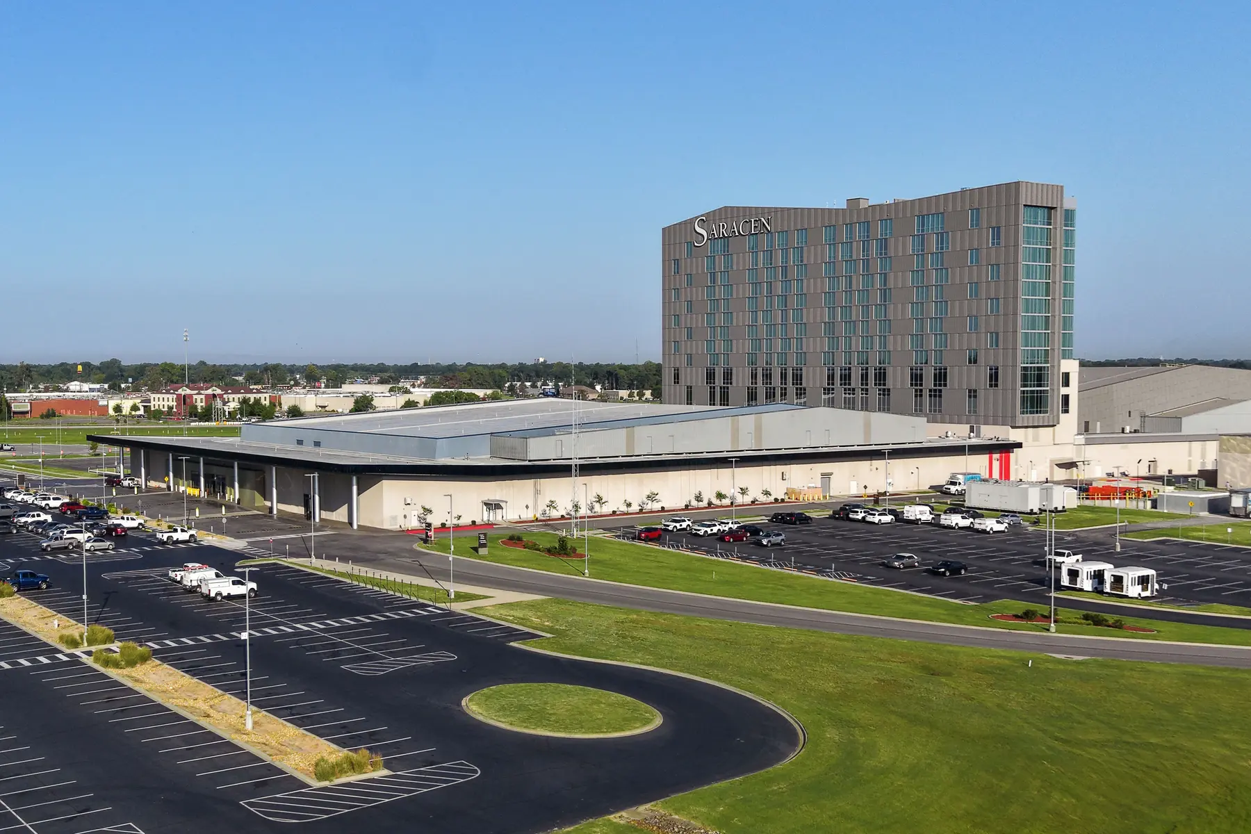 Luftaufnahme des Saracen Casino Resort Gebäudekomplexes mit Hotel und Parkplatz unter blauem Himmel.