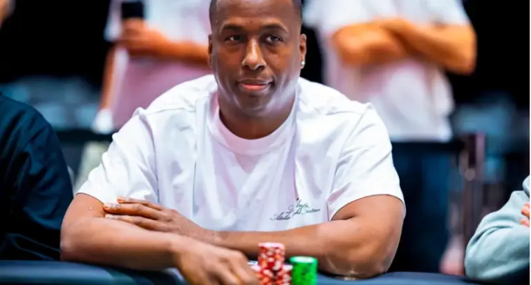 Pokerspelare i vit t-shirt sitter vid ett pokerbord med marker framför sig under en turnering.