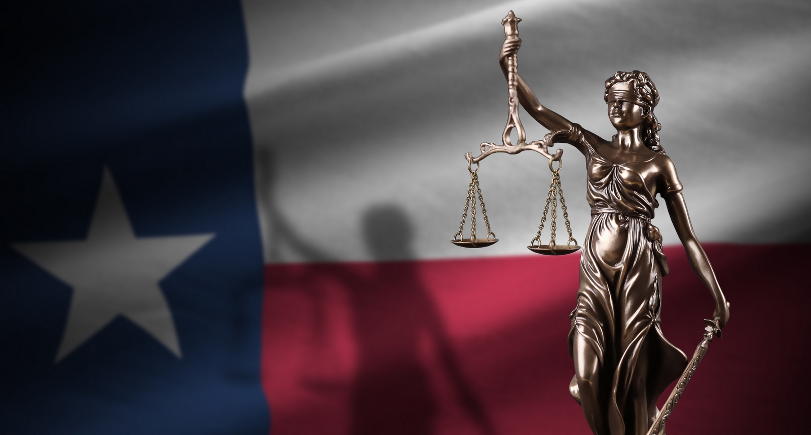 A Texas flag with a statue of Lady Justice in the foreground.